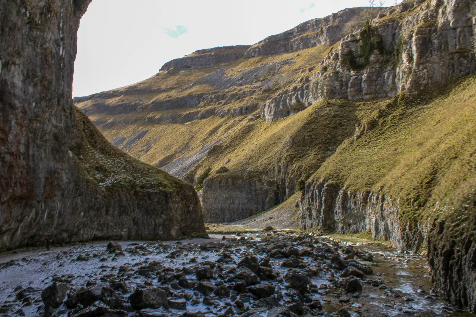 The narrow entrance to Gordale Scar, with overhanging limestone cliffs above a rocky streambed