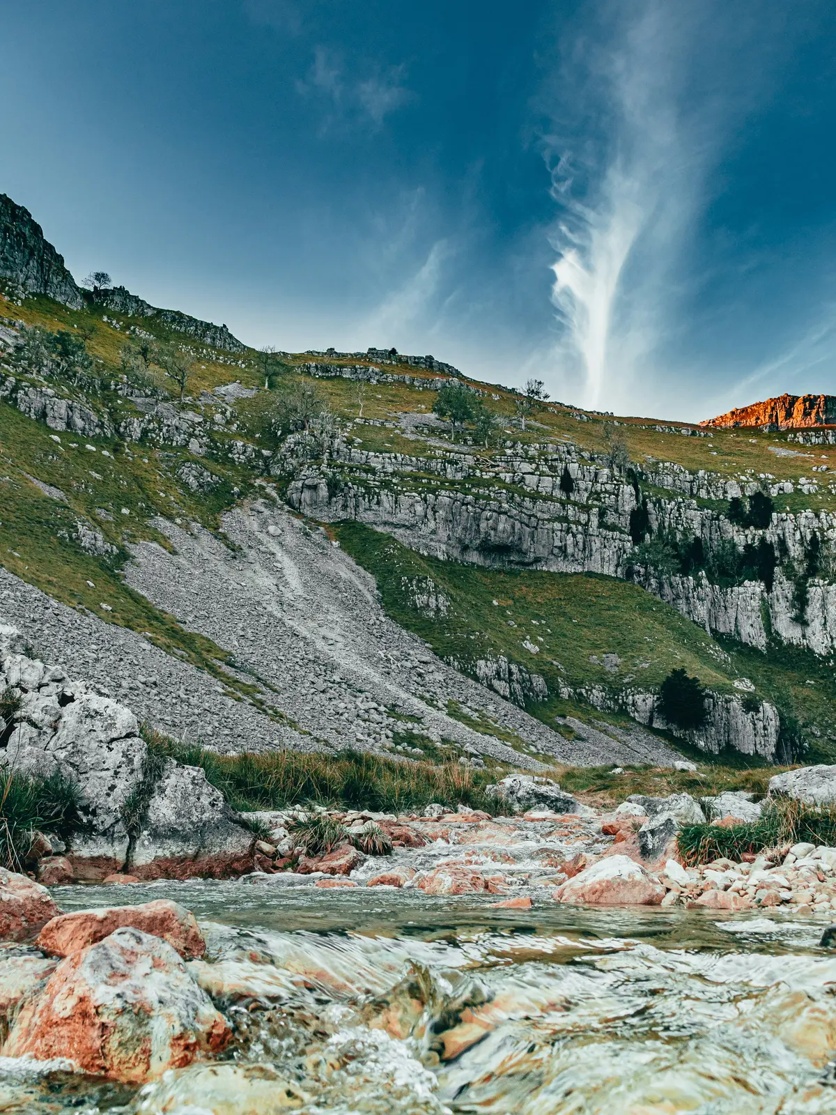 A stream flowing through limestone scree and scar near Malham, beneath a dramatic sky